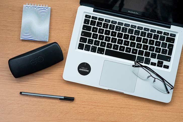 briller, en penn, et brilleetui og en PC på en benk